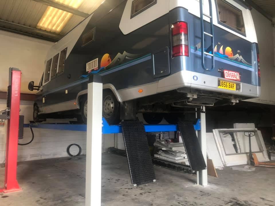 A motorhome raised on the blue four-post lift inside the workshop
